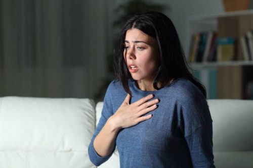 A woman putting her hand on her chest as she experiences some pain and difficulty breathing